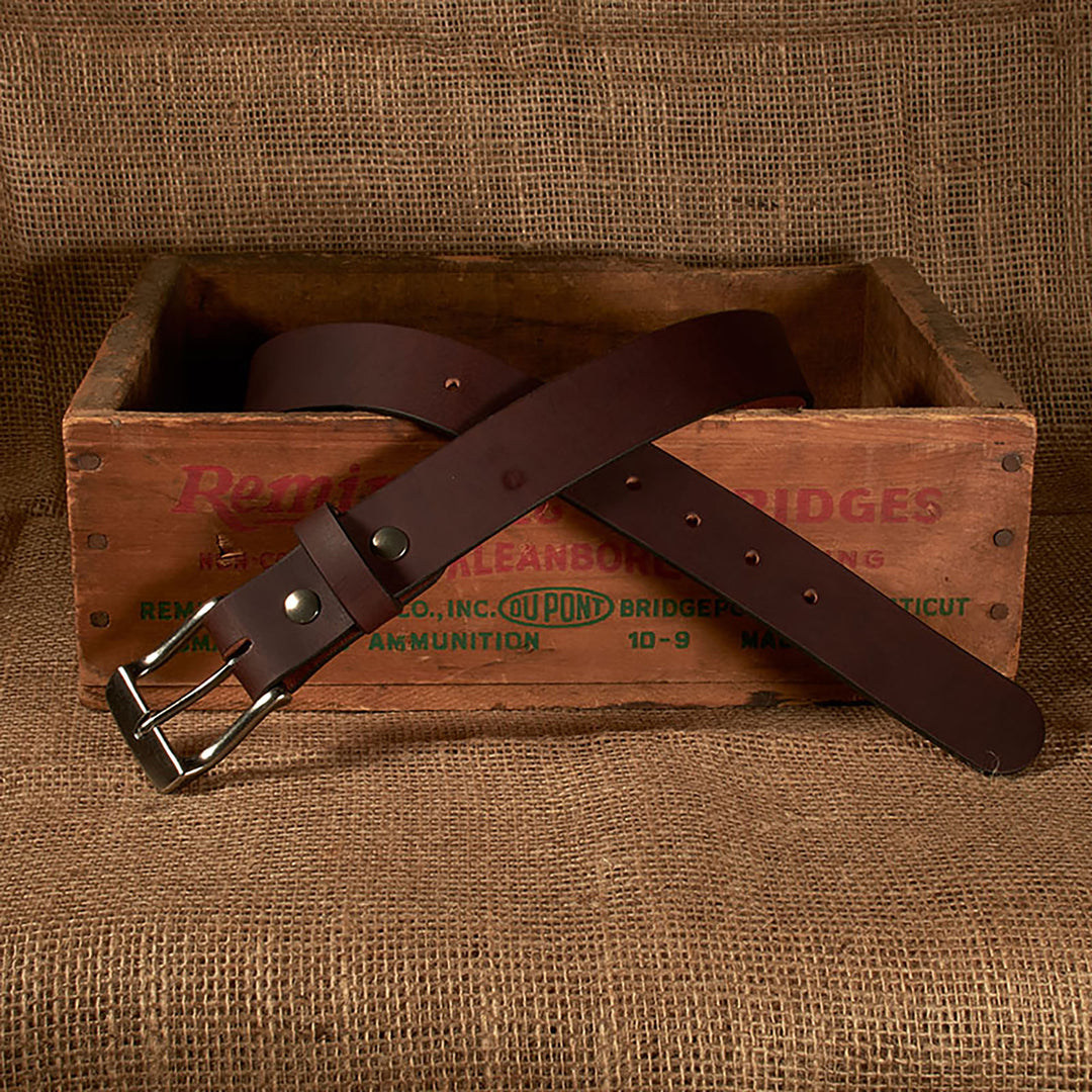 Brown leather belt with silver buckle on a rustic wooden box and burlap background