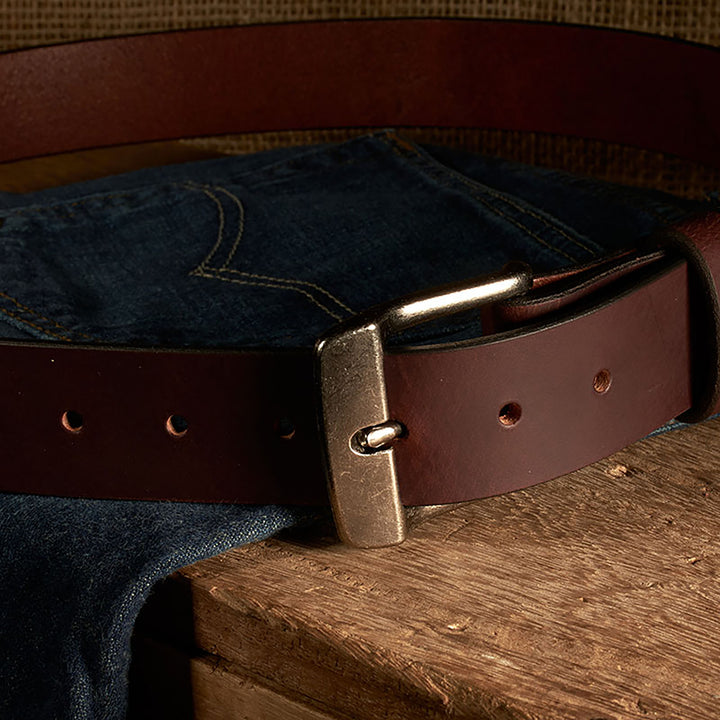 Brown leather belt with brass buckle on a wooden surface