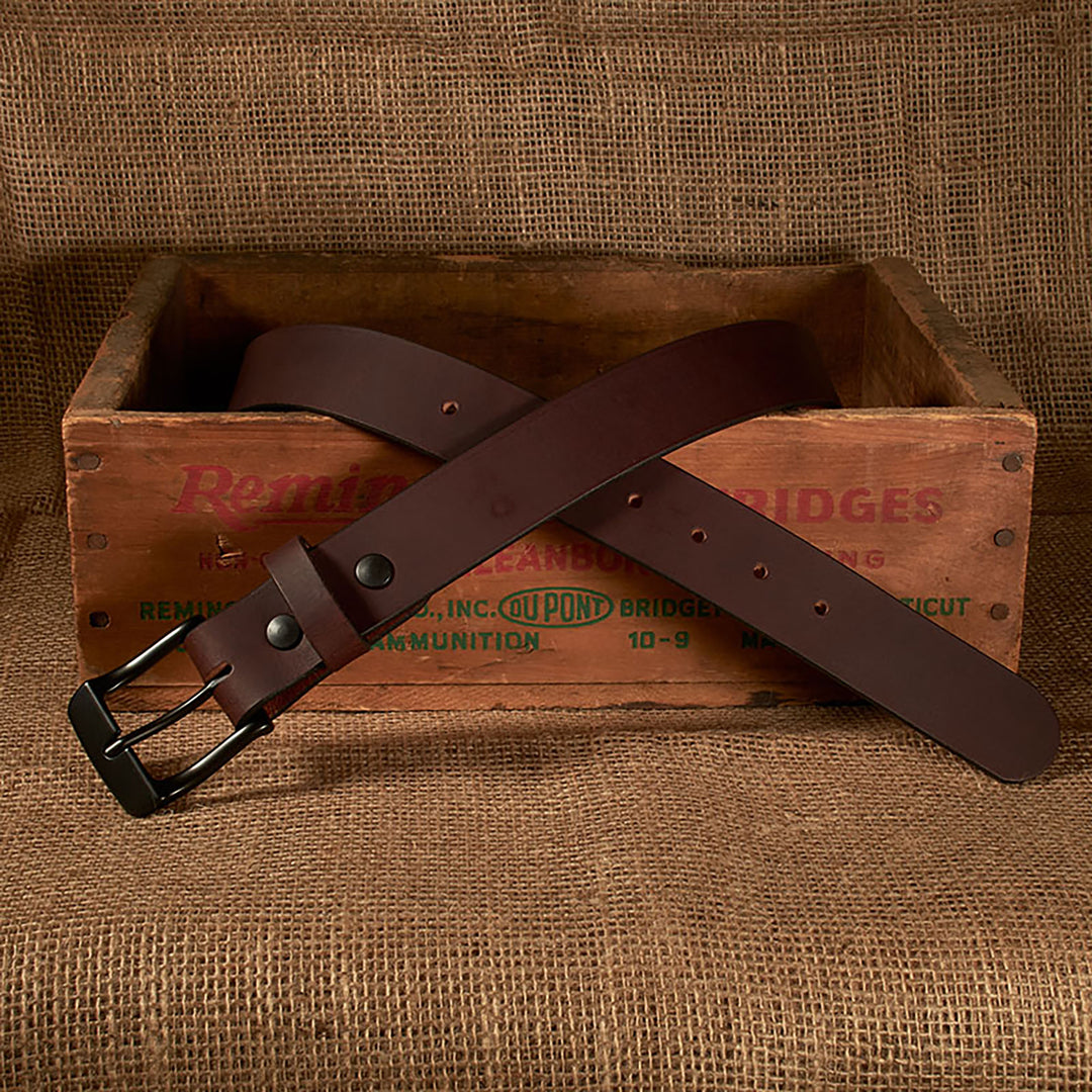 Brown leather belt with a black buckle on a wooden crate with 'Remington' branding.
