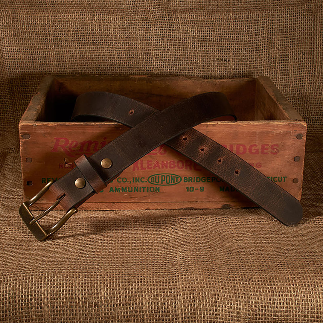 Brown leather belt with brass buckle on a vintage wooden crate against a textured brown background