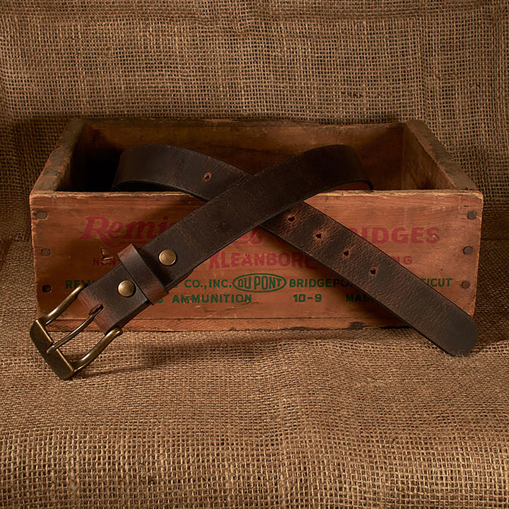 Brown leather belt with brass buckle on a vintage wooden crate against a textured brown background