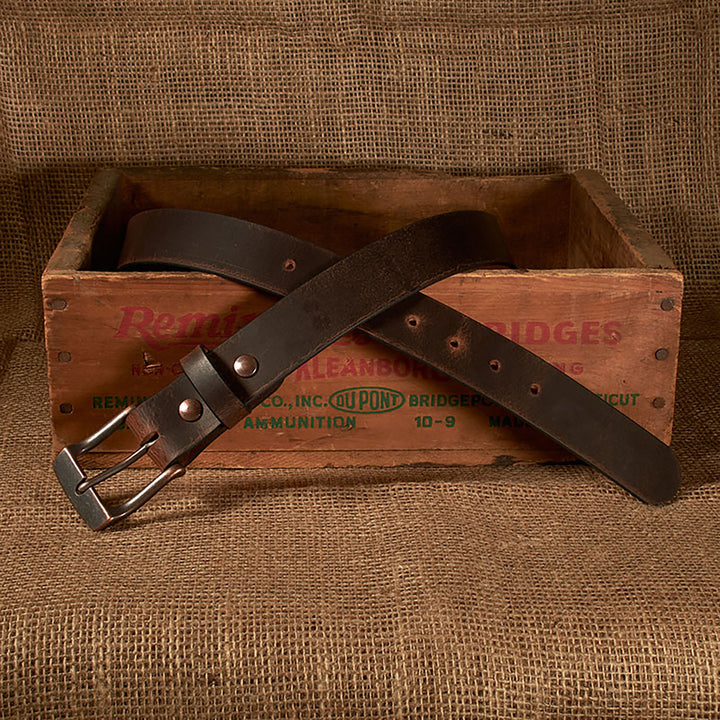 Brown leather belt with metal buckle on a wooden box against a brown fabric background