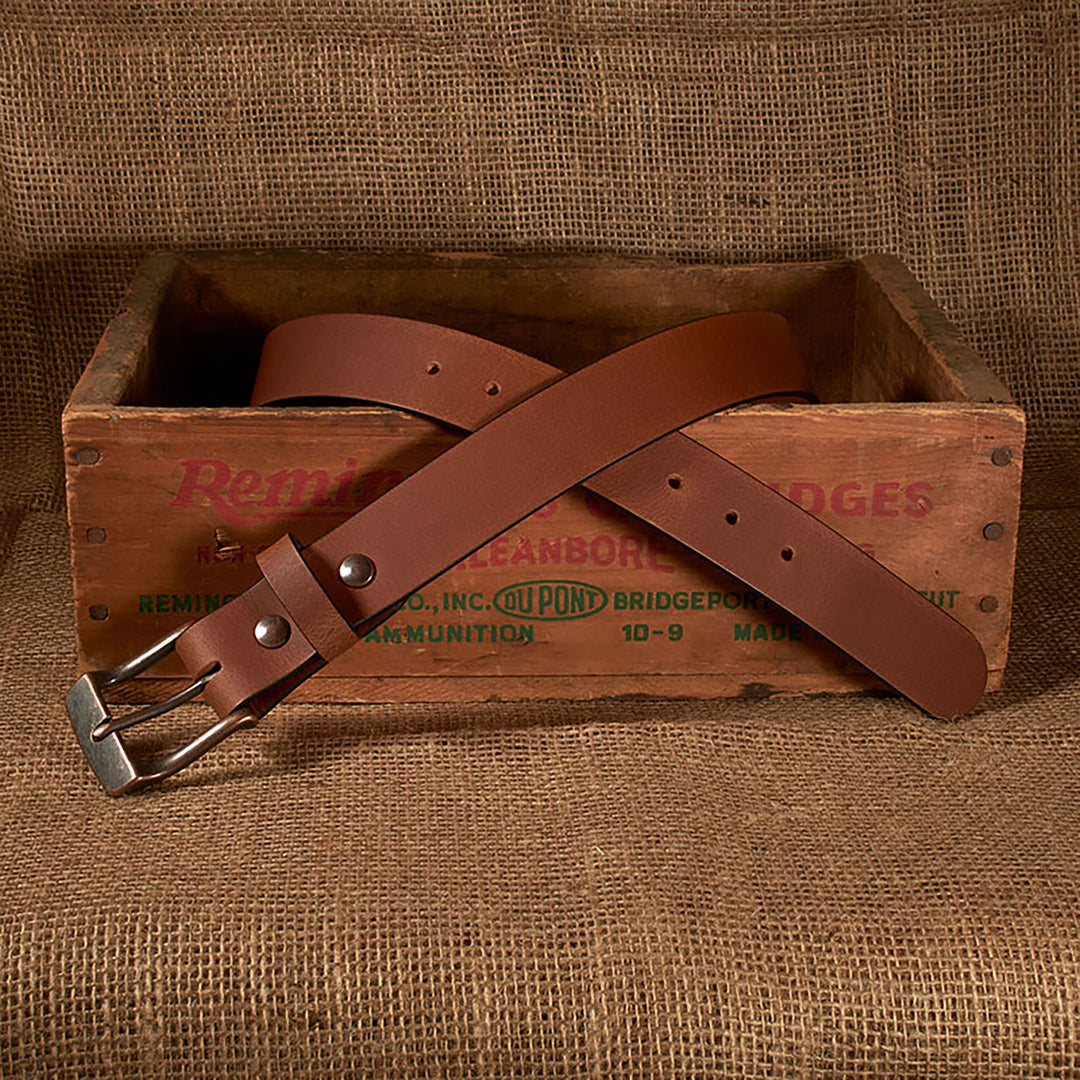 Brown leather belt with silver buckle on a wooden box labeled 'Remington'.