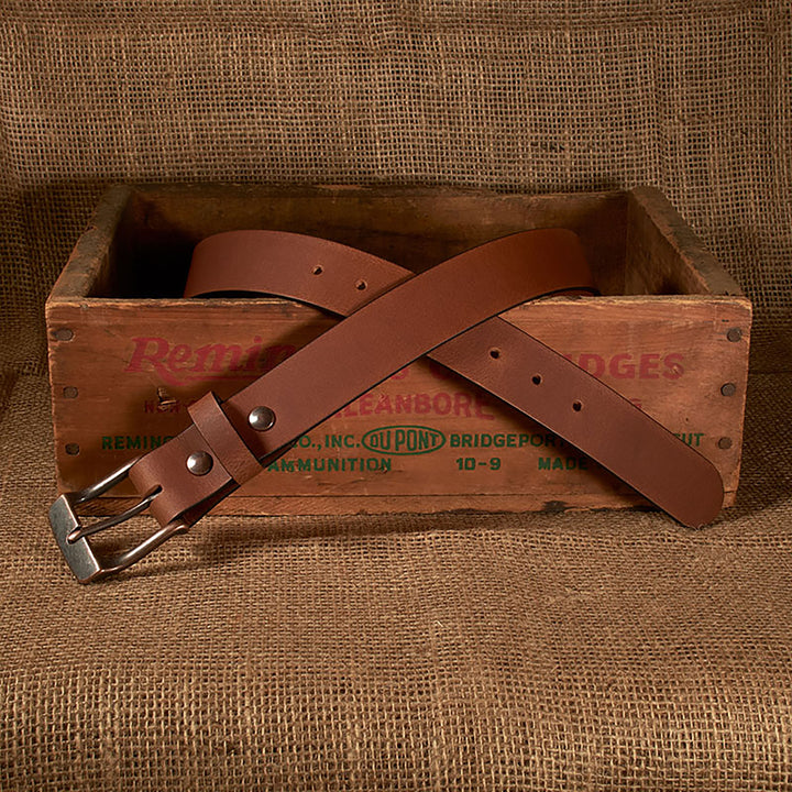 Brown leather belt with silver buckle on a wooden box labeled 'Remington'.