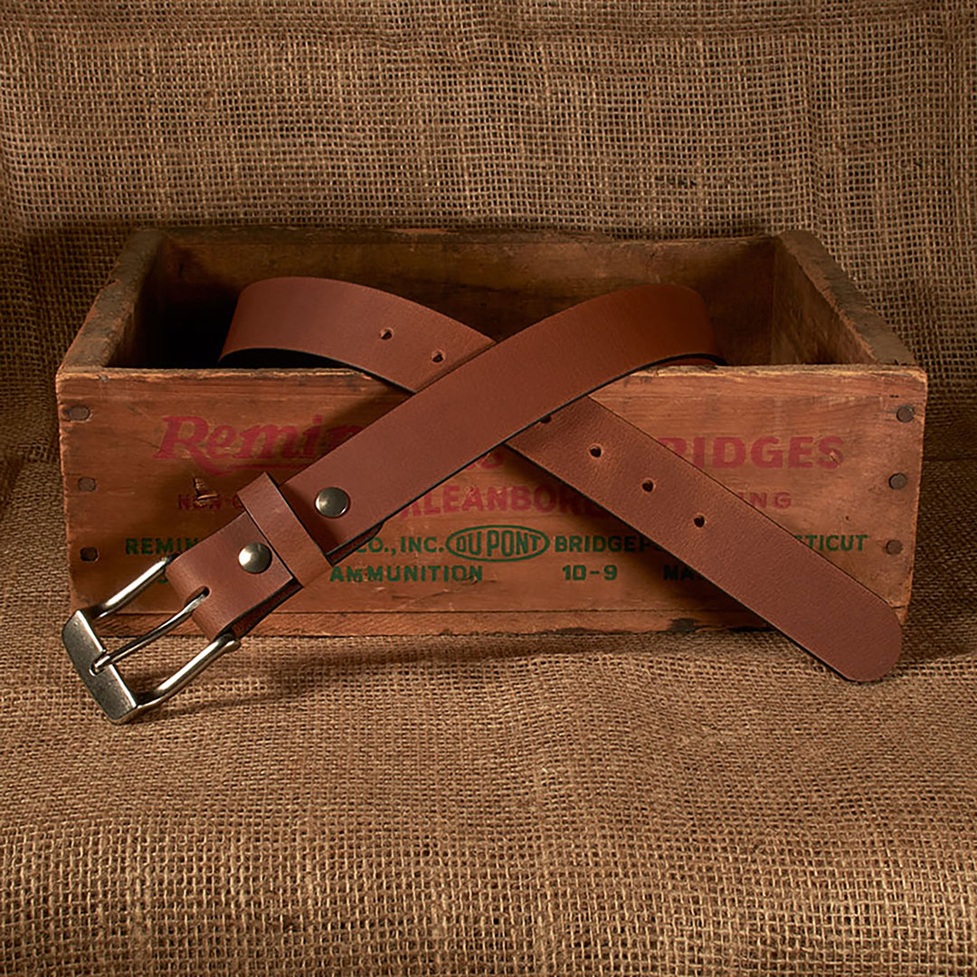 Brown leather belt with silver buckle on a wooden crate with 'Remington' branding.