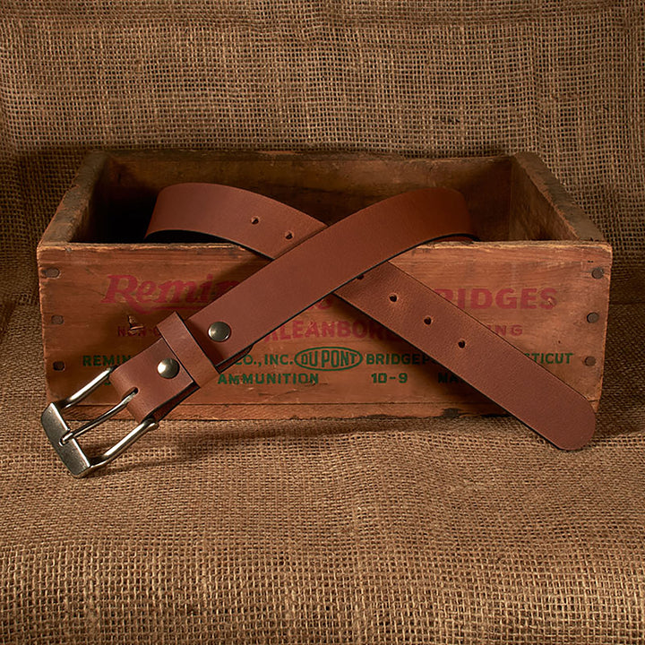 Brown leather belt with silver buckle on a wooden crate with 'Remington' branding.