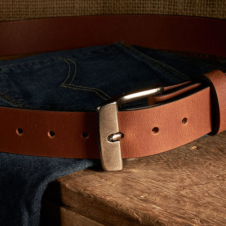 Brown leather belt with a silver buckle on a denim jacket against a wooden surface