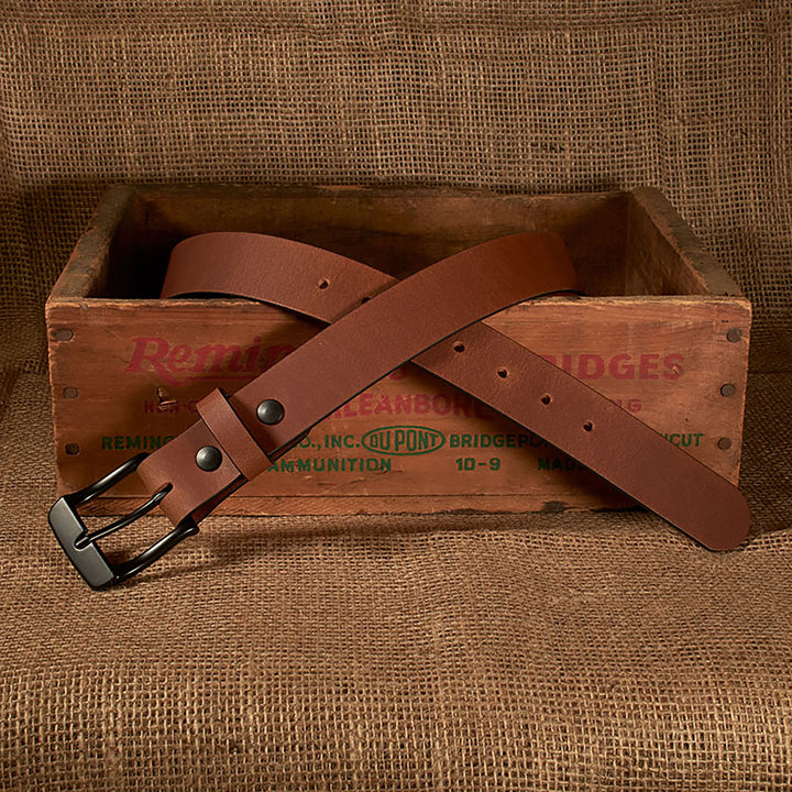 Brown leather belt with a black buckle on a rustic wooden box against a burlap background