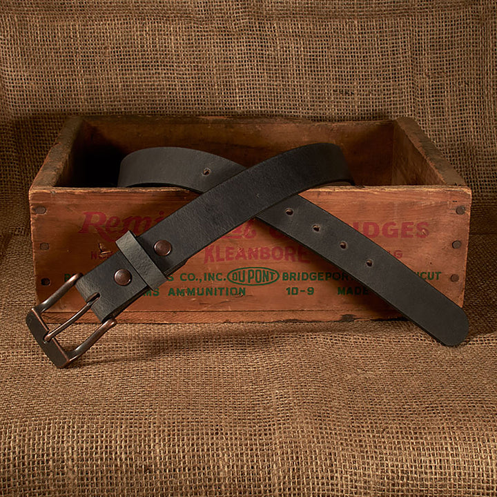 Black leather belt with brass buckle on a rustic wooden crate against a burlap background