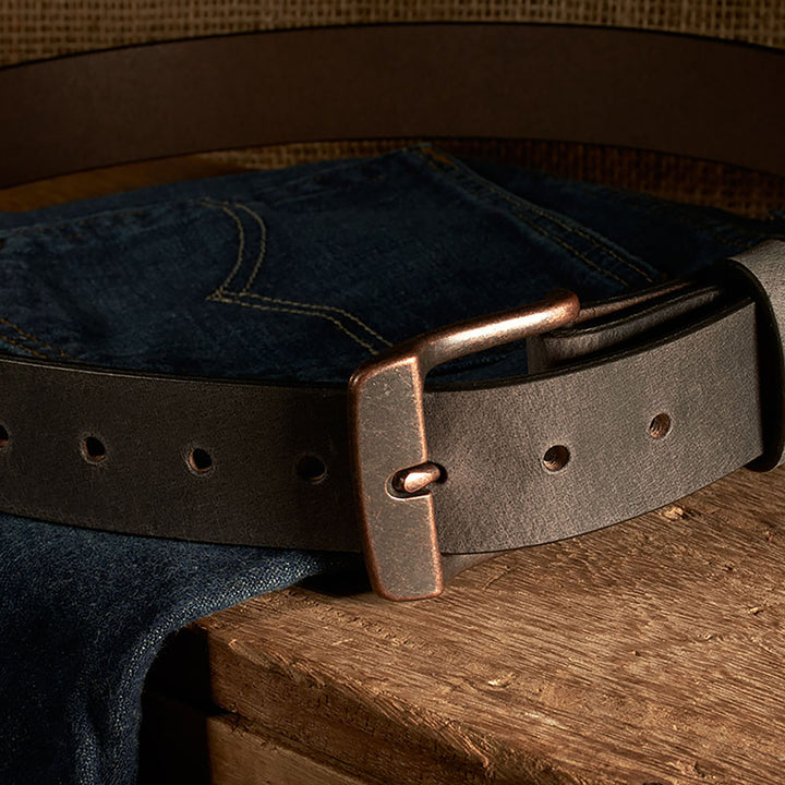 Brown leather belt with brass buckle on a wooden surface