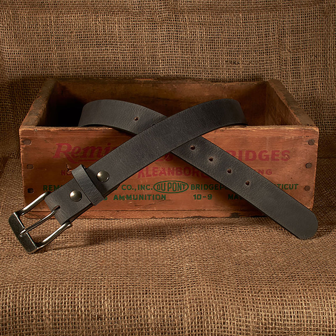 Dark leather belt with metal buckle on a rustic wooden crate against a burlap background