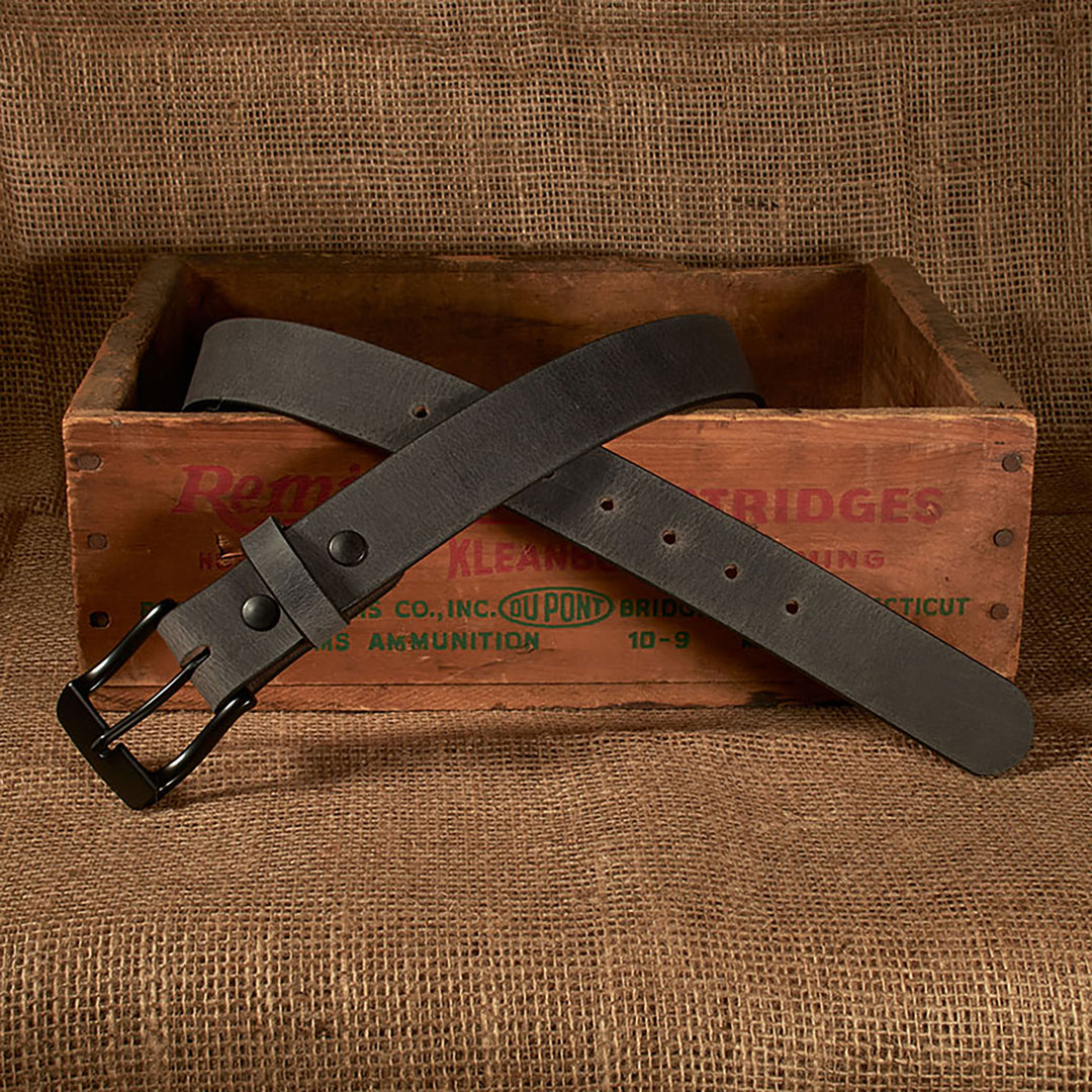 Black leather belt with a black buckle on a rustic wooden crate with 'Bridges' branding.