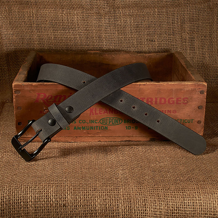 Black leather belt with a black buckle on a rustic wooden crate with 'Bridges' branding.