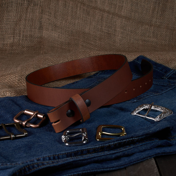 Brown leather belt with various metal buckles on a denim surface.