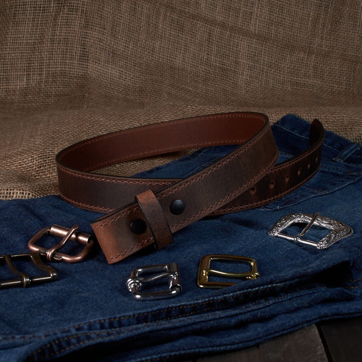 Brown leather belt with various metal buckles on a denim surface