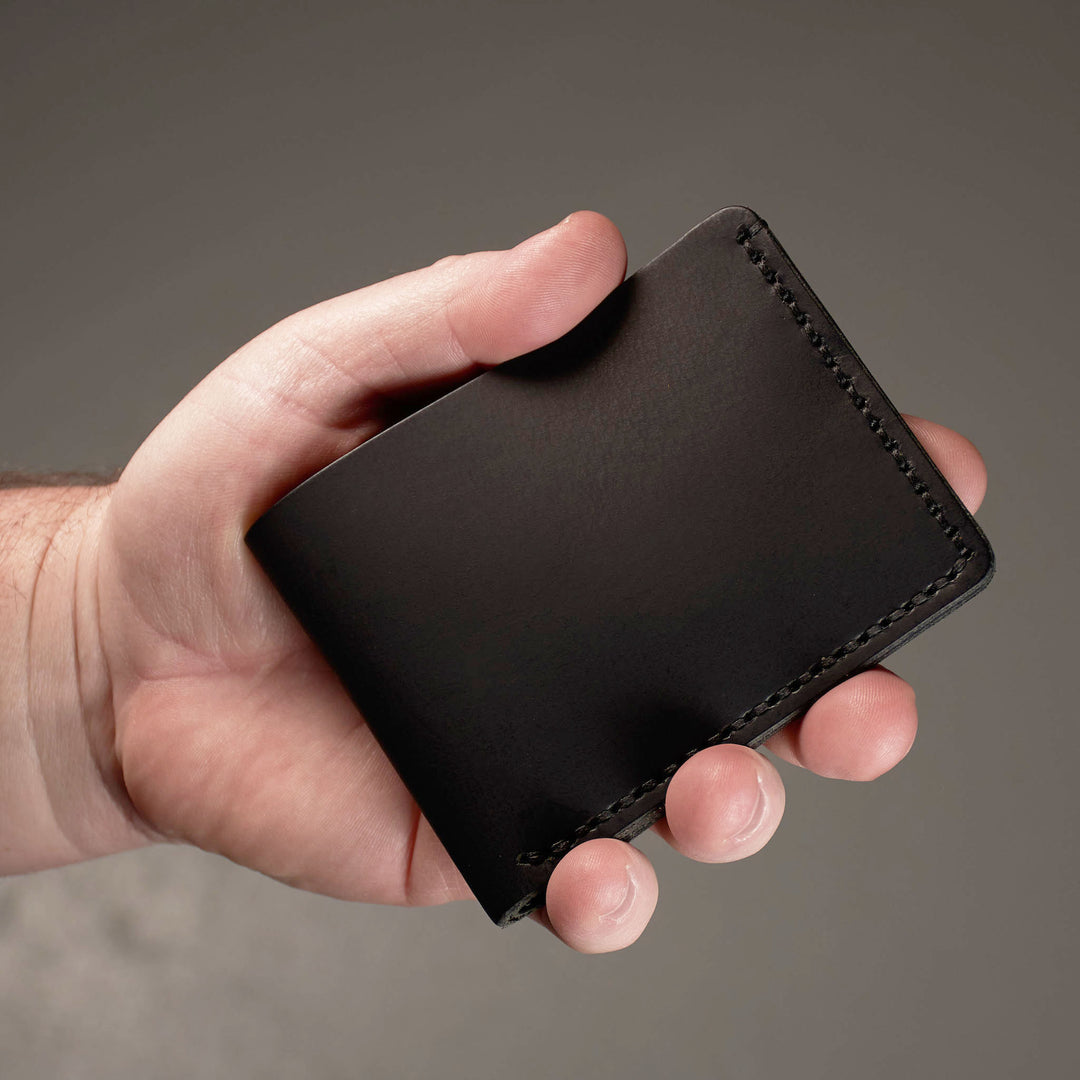 Hand holding a black leather wallet against a gray background