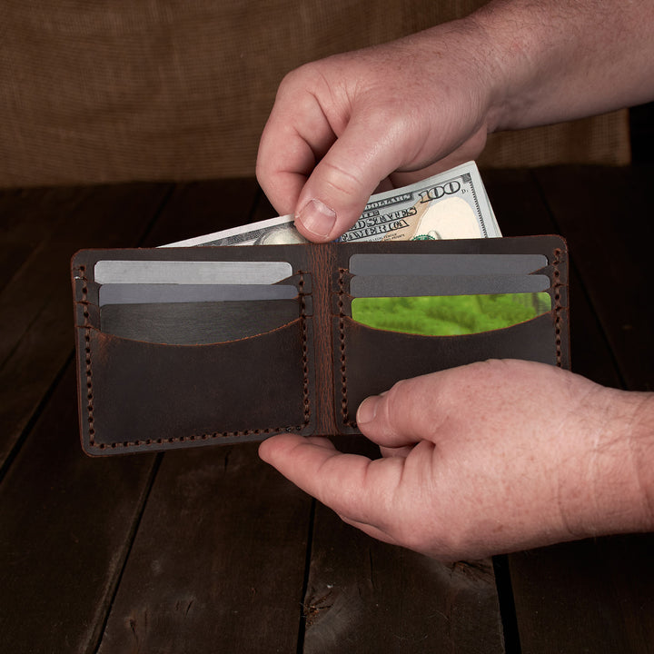 Person holding a brown leather wallet with money and cards on a wooden surface