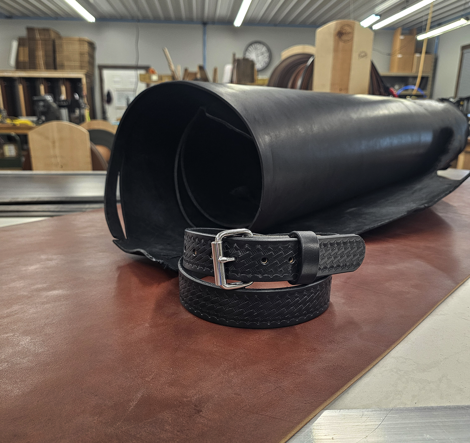 Black leather belt on a wooden surface with a large roll of black material in the background.