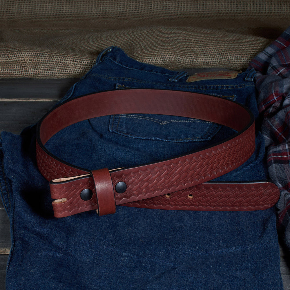 Red leather belt on a person wearing blue jeans and a plaid shirt against a wooden background