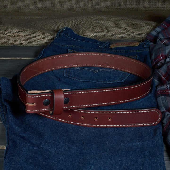 Brown leather belt on a blue denim shirt with plaid fabric in the background