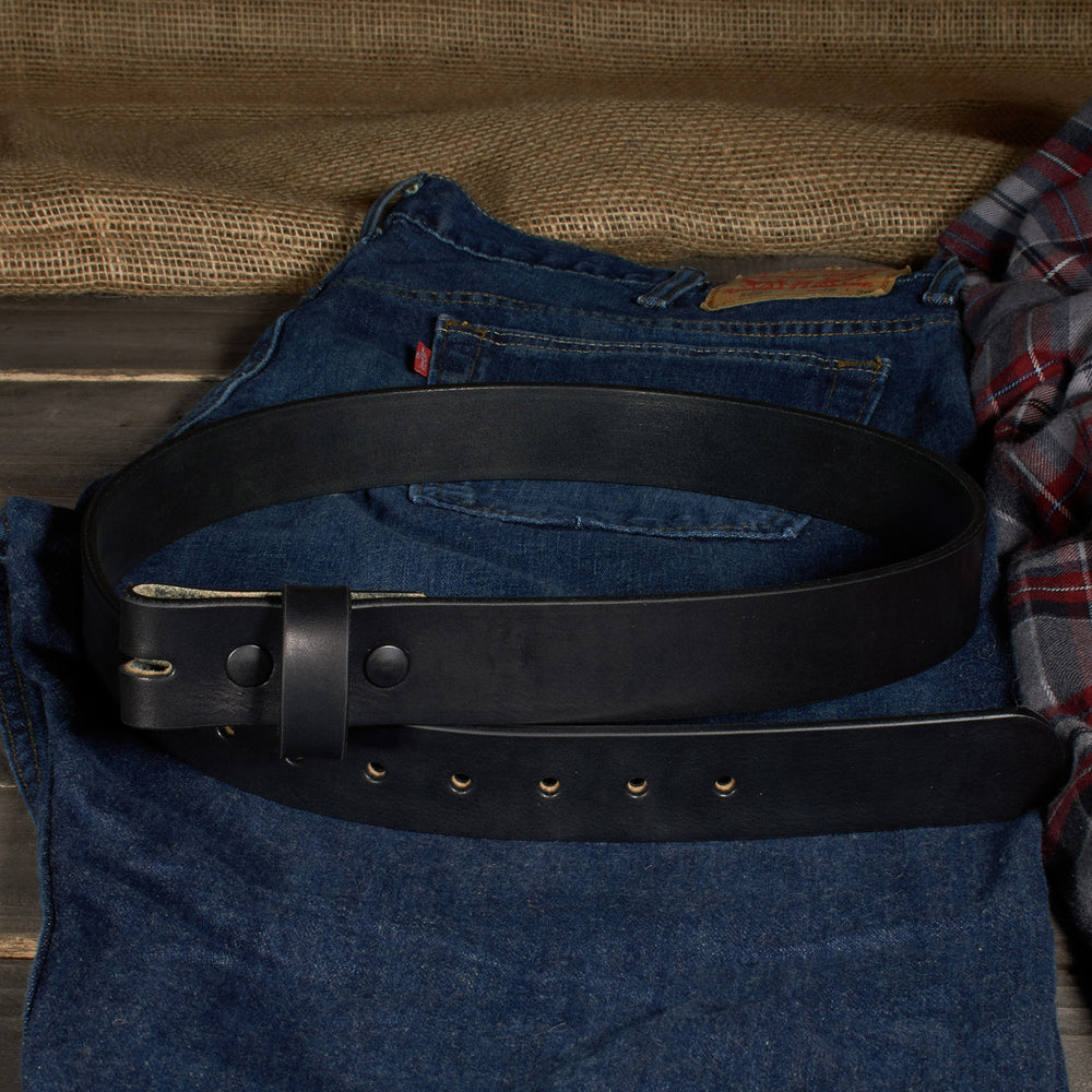 Black leather belt on a pair of blue jeans with a plaid shirt in the background.
