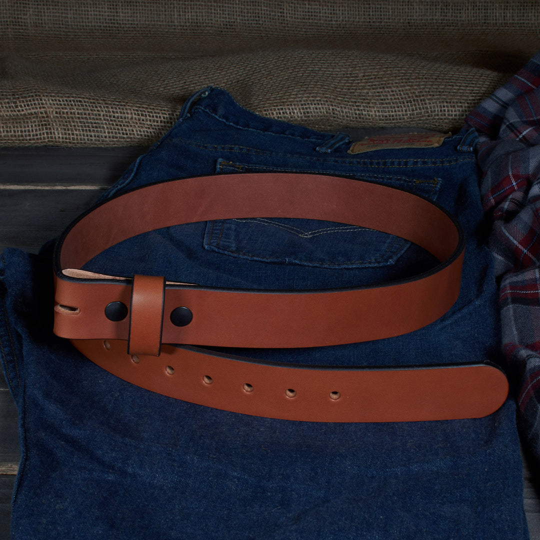 Brown leather belt on a blue denim jacket with a plaid shirt in the background.