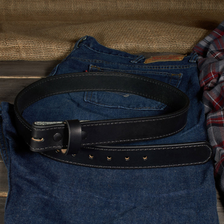 Black belt on a pair of blue jeans with a plaid shirt in the background.