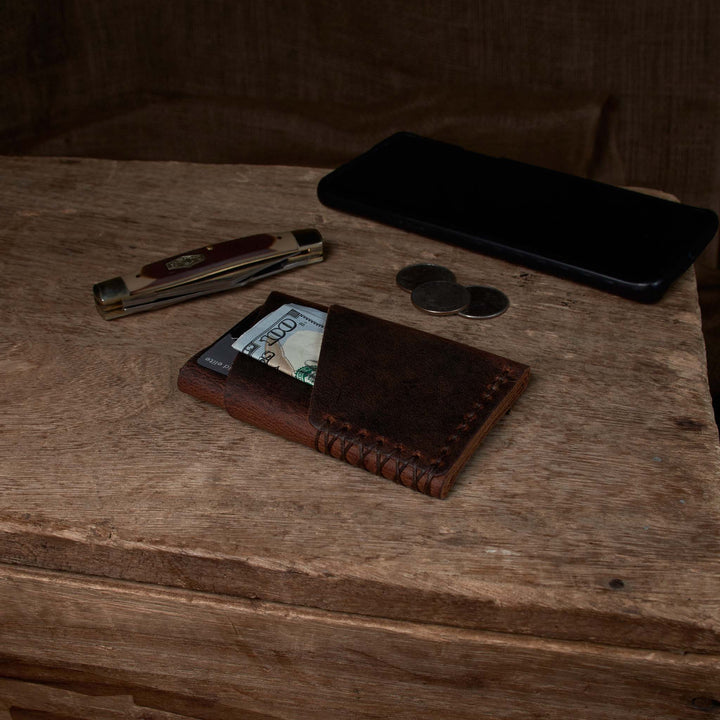 Brown leather wallet with money, phone, and knife on a wooden surface