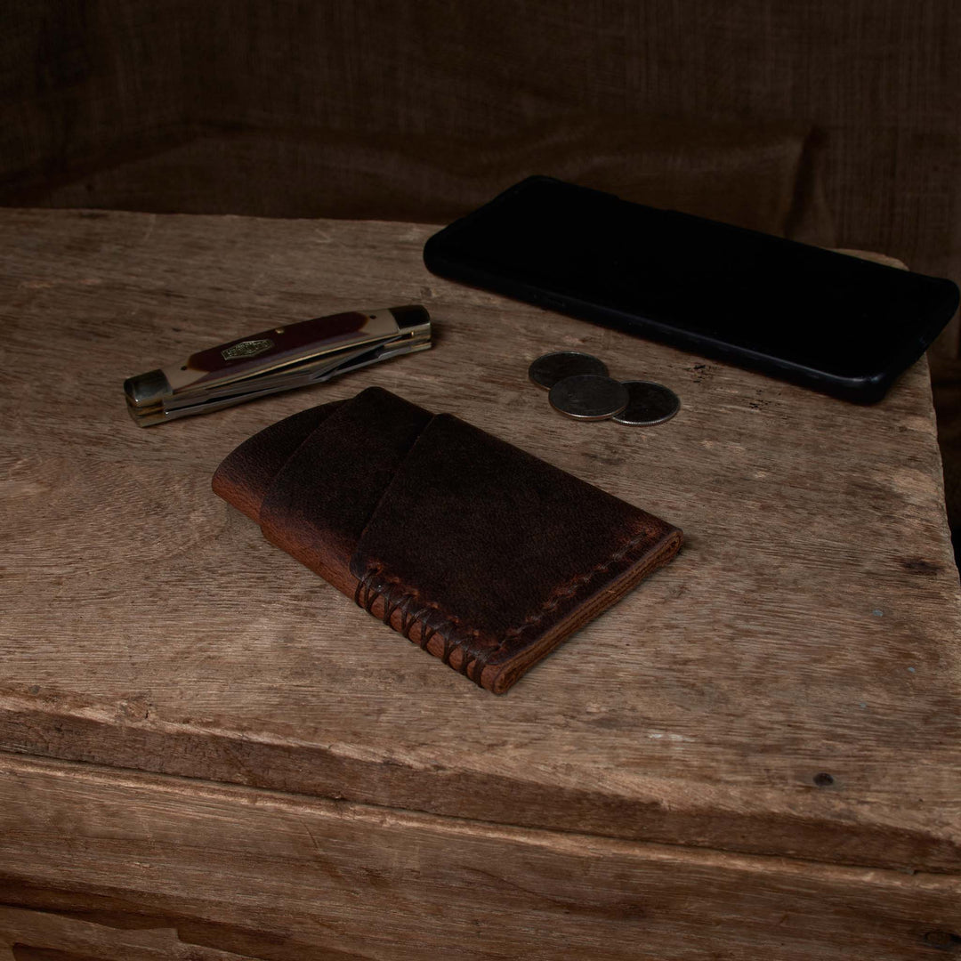 Brown leather wallet, knife, coins, and phone on a wooden surface