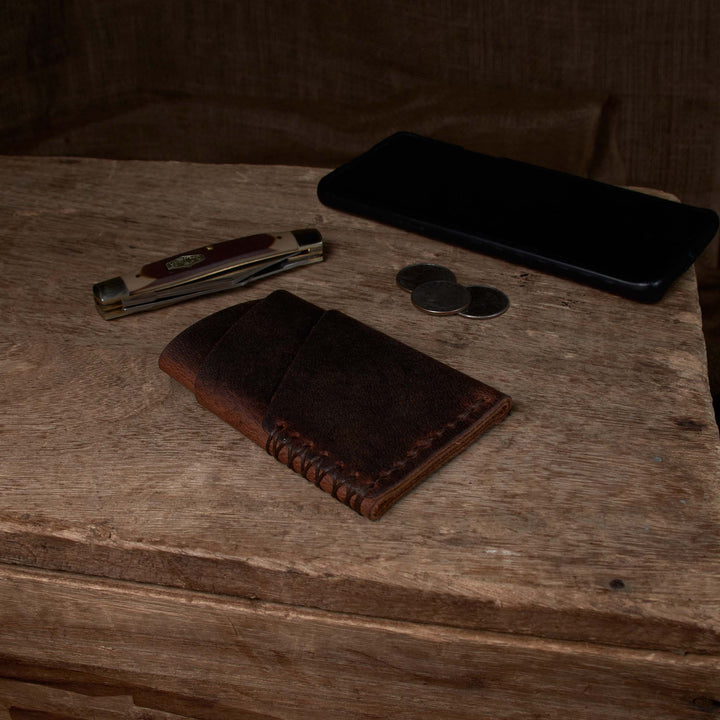 Brown leather wallet, knife, coins, and phone on a wooden surface