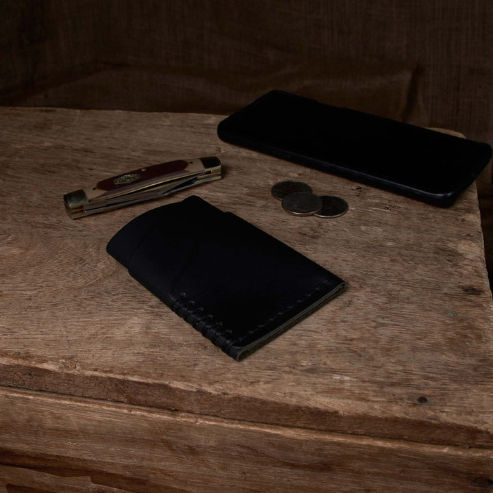 Black wallet, phone, and coins on a wooden surface
