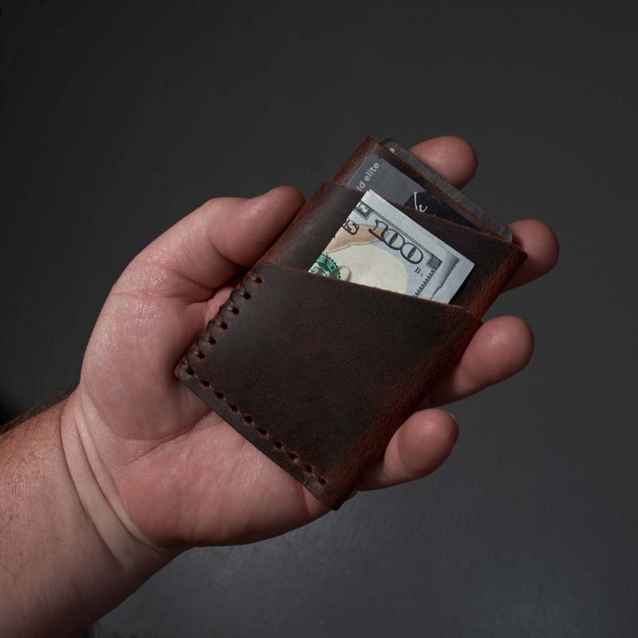 Hand holding a brown leather wallet with money against a dark background