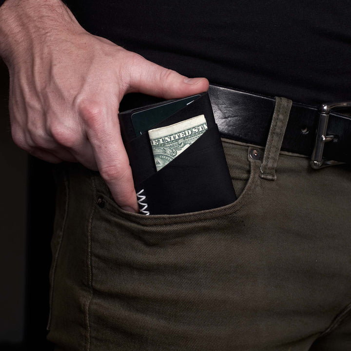 Person placing money into a black wallet held in front of a dark background