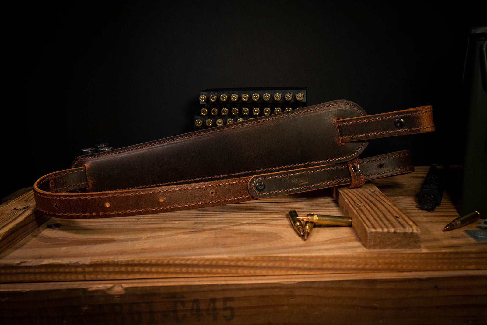 Handmade vintage brown leather rifle sling by Nohma Leather shown with ammunition on a wooden crate.